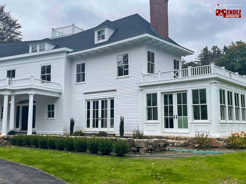 A large white house with a new roof and sunroom, showcasing exterior renovation by Mendez Contractor Inc in Lynn, MA
