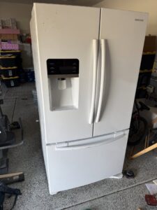 A large white refrigerator in a garage, ready for appliance removal by Kern County Junk Removal in Bakersfield, CA.