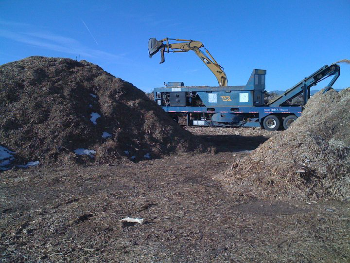 A large wood chipper machine next to piles of wood chips, demonstrating services by Aesthetic Tree Service in Denver, CO.