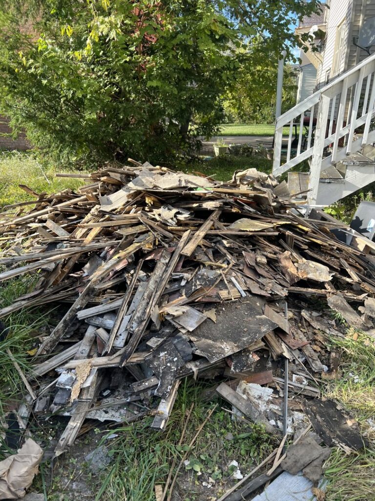 A large pile of wood debris and construction waste next to a house, ready for removal by Prestige Junk Removal & Hauling in Detroit, MI