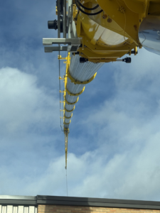 A large yellow crane boom extends high above a building, showcasing construction work by BURT crane & rigging in Green Island, NY.