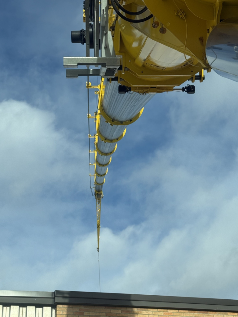 A large yellow crane boom extends high above a building, showcasing construction work by BURT crane & rigging in Green Island, NY.