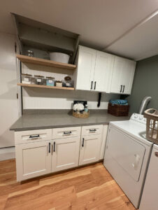A renovated laundry room with new white cabinets, a grey countertop, and shelving by Garrett Group Construction in Philadelphia, PA.