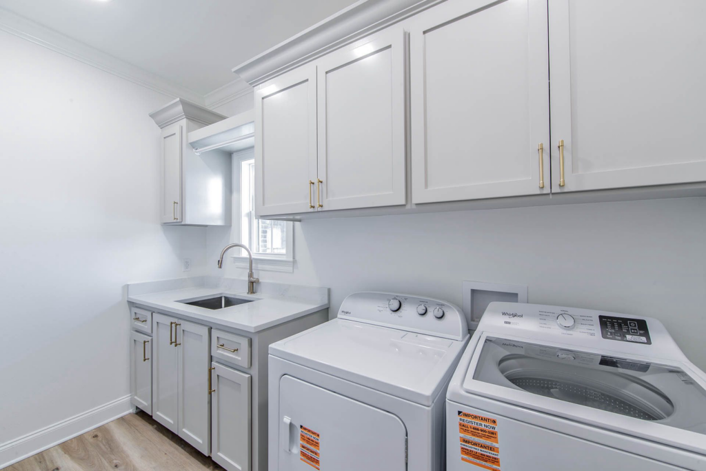 A newly installed laundry room with white cabinets, sink, washer, and dryer by LP Home Builders in Houma, LA.