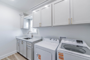 A newly installed laundry room with white cabinets, sink, washer, and dryer by LP Home Builders in Houma, LA.