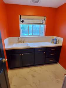 A vibrant orange laundry room remodel with new dark cabinets, white sink, and tiled floor by Lilac Remodel Spokane in Spokane Valley, WA.