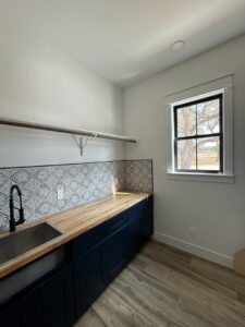 A beautifully remodeled laundry room with custom dark cabinets, a wood countertop, and a patterned backsplash, by Roaring Lion Renovations, LLC in Houston, TX.