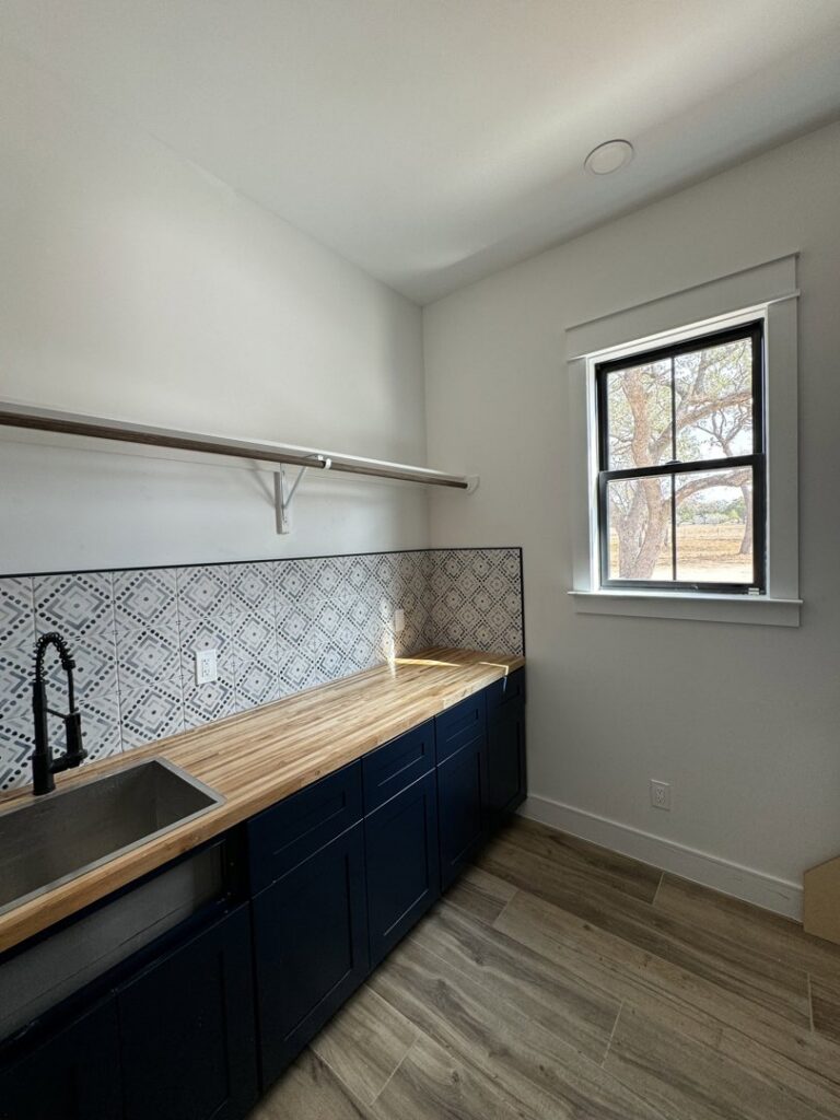 A beautifully remodeled laundry room with custom dark cabinets, a wood countertop, and a patterned backsplash, by Roaring Lion Renovations, LLC in Houston, TX.