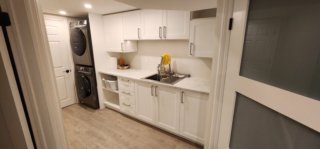 A newly remodeled laundry room with white cabinets, a sink, and stacked washer and dryer by NP General Contracting in Austin, TX.
