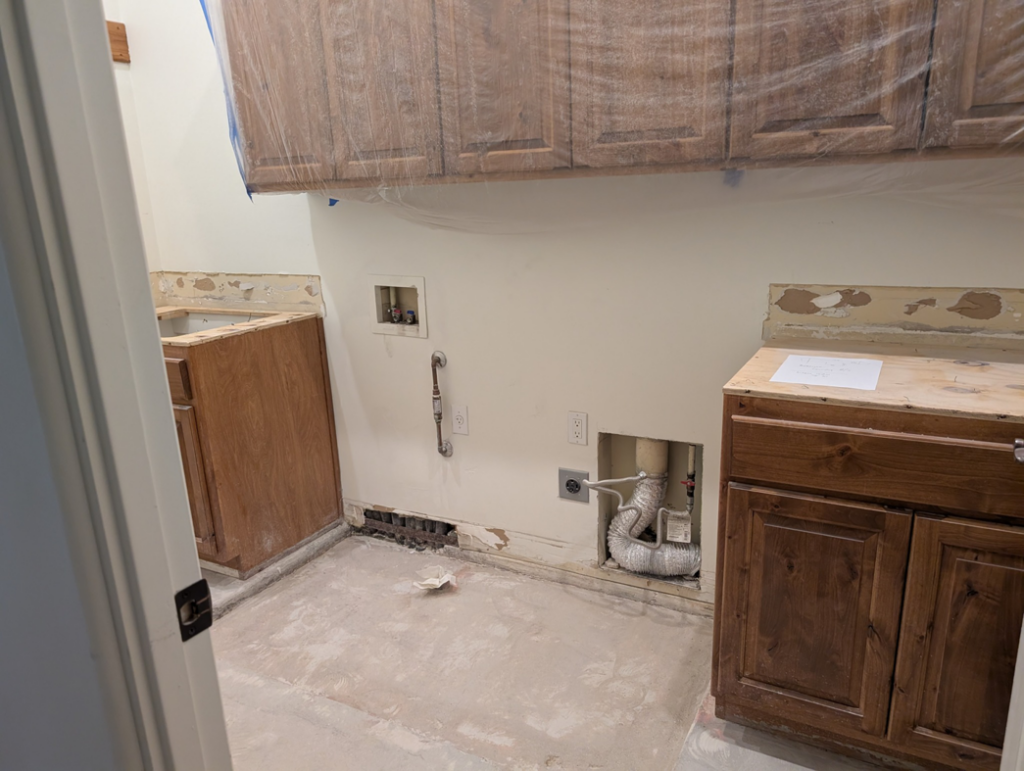 Laundry room under renovation with exposed plumbing and an unfinished floor by Prestwick Custom Homes in Gilbert, AZ