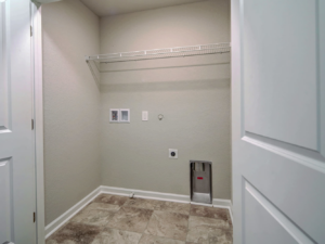 An empty laundry room with an installed wire shelf and utility hookups by GTB Construction in Portsmouth, VA.