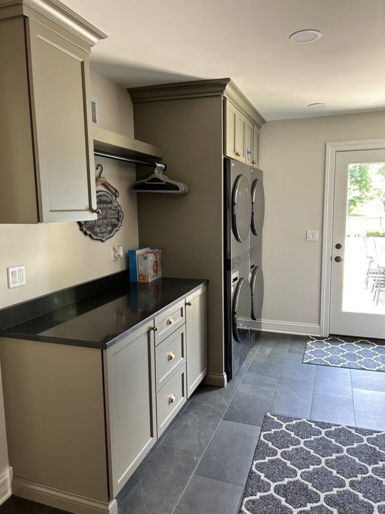 A renovated laundry room with stacked washer and dryer, custom cabinets, and a countertop by Synergy Builders in West Chicago, IL.
