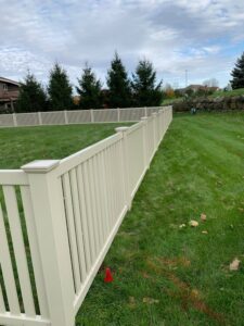 A light-colored vinyl fence installed on a sloped grassy area by Badger Vinyl Products in Madison, WI.