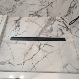 A sleek linear shower drain installed in a marble-look tiled shower floor by Ensotile - Atlanta Bathroom Remodeling in Stone Mountain, GA