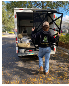 A Litter Hitters employee loading a large metal frame into a junk removal truck in Jacksonville, FL.