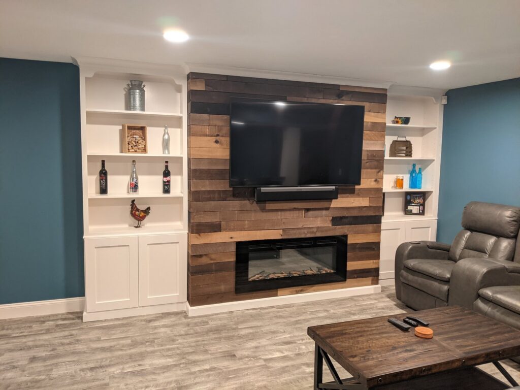 A finished living room with custom built-in shelves, a mounted TV, and an electric fireplace installed by BizMick Construction in Coventry, RI.