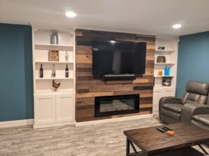 A finished living room with custom built-in shelves, a mounted TV, and an electric fireplace installed by BizMick Construction in Coventry, RI.