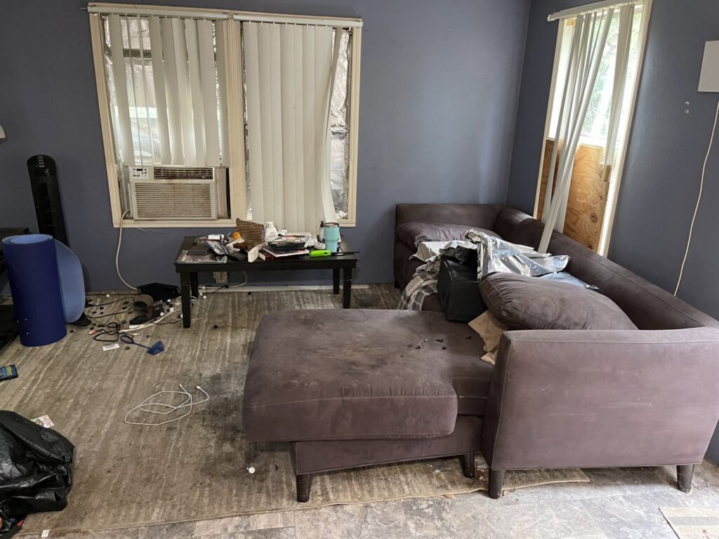 A cluttered living room with old furniture and debris on the floor, indicating a cleanout service by G.I. HAUL Austin, TX.
