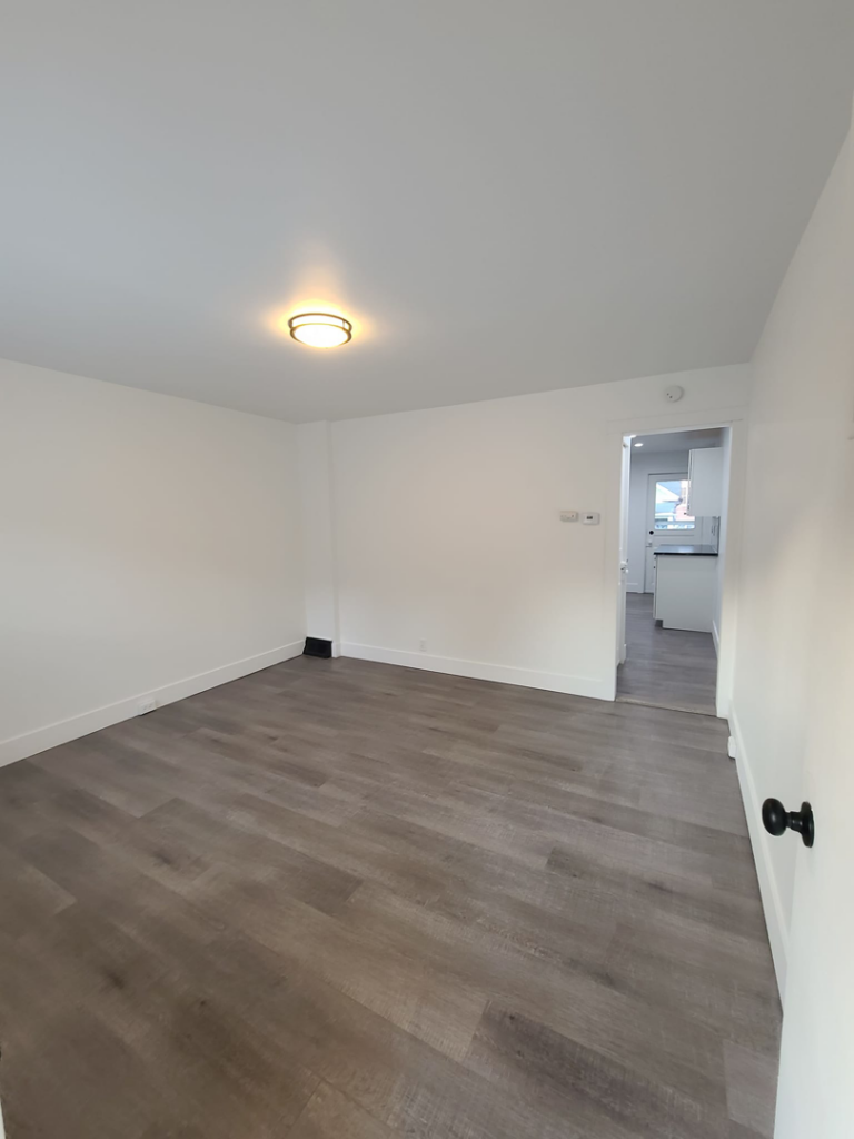 A spacious living room with dark laminate flooring and white walls, a project by Modern Image Construction LLC in El Paso, TX