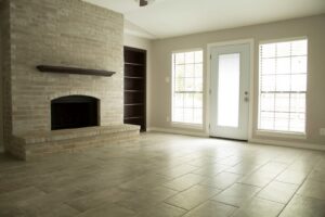 A newly renovated living room featuring a brick fireplace, modern tiled flooring, and large windows, completed by Custer Remodeling in Plano, TX.
