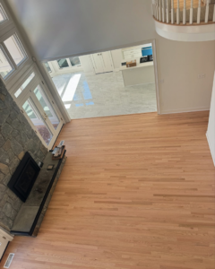 Spacious living room with newly installed light hardwood floors and a stone fireplace by International Wood Floors in Gaithersburg, MD