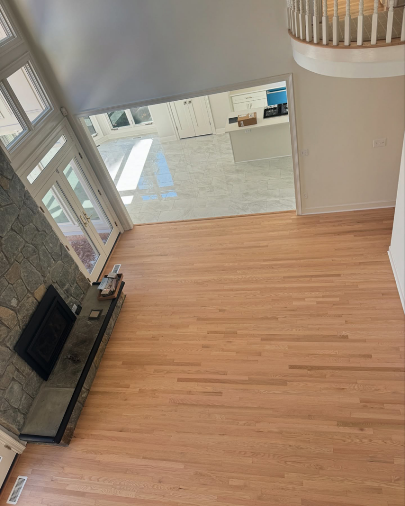 Spacious living room with newly installed light hardwood floors and a stone fireplace by International Wood Floors in Gaithersburg, MD