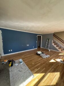 A living room with a partially painted blue wall and painting supplies, showing an interior painting job in progress by Quinonez Painting & Renovations LLC in Providence, RI.