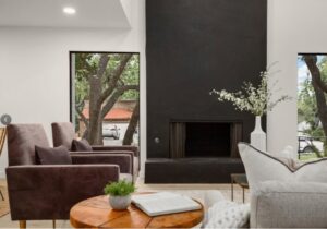 A renovated living room showcasing a modern dark fireplace and large windows by Proper 3 Renovations in Austin, TX
