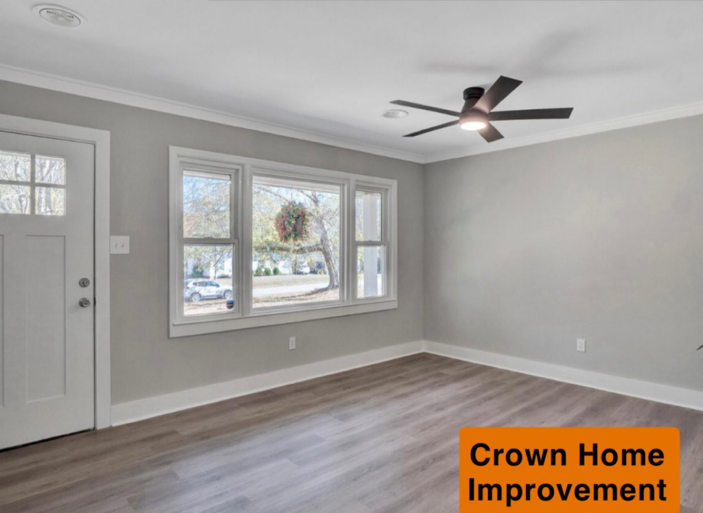 A renovated living room with new flooring, a ceiling fan, and a new front door installed by Crown Home Improvements in Charlotte, NC
