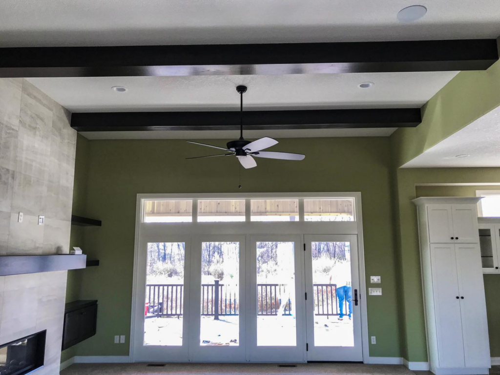 A living room with freshly painted walls, a new ceiling fan, and exposed beams by Grabill Painting and Drywall in Fort Wayne, IN.