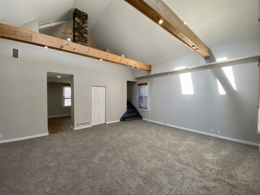 A spacious living room after renovation, featuring new carpet and exposed wooden beams by RT Property Services in Allendale, MI