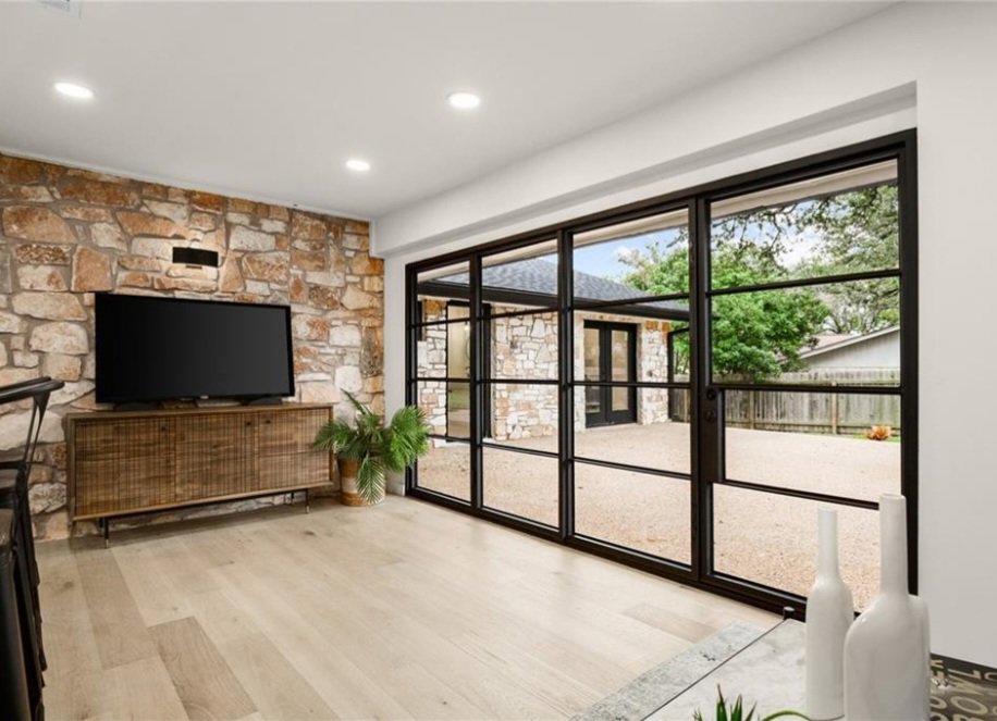 A renovated living room with a natural stone accent wall and large glass patio doors by Proper 3 Renovations in Austin, TX
