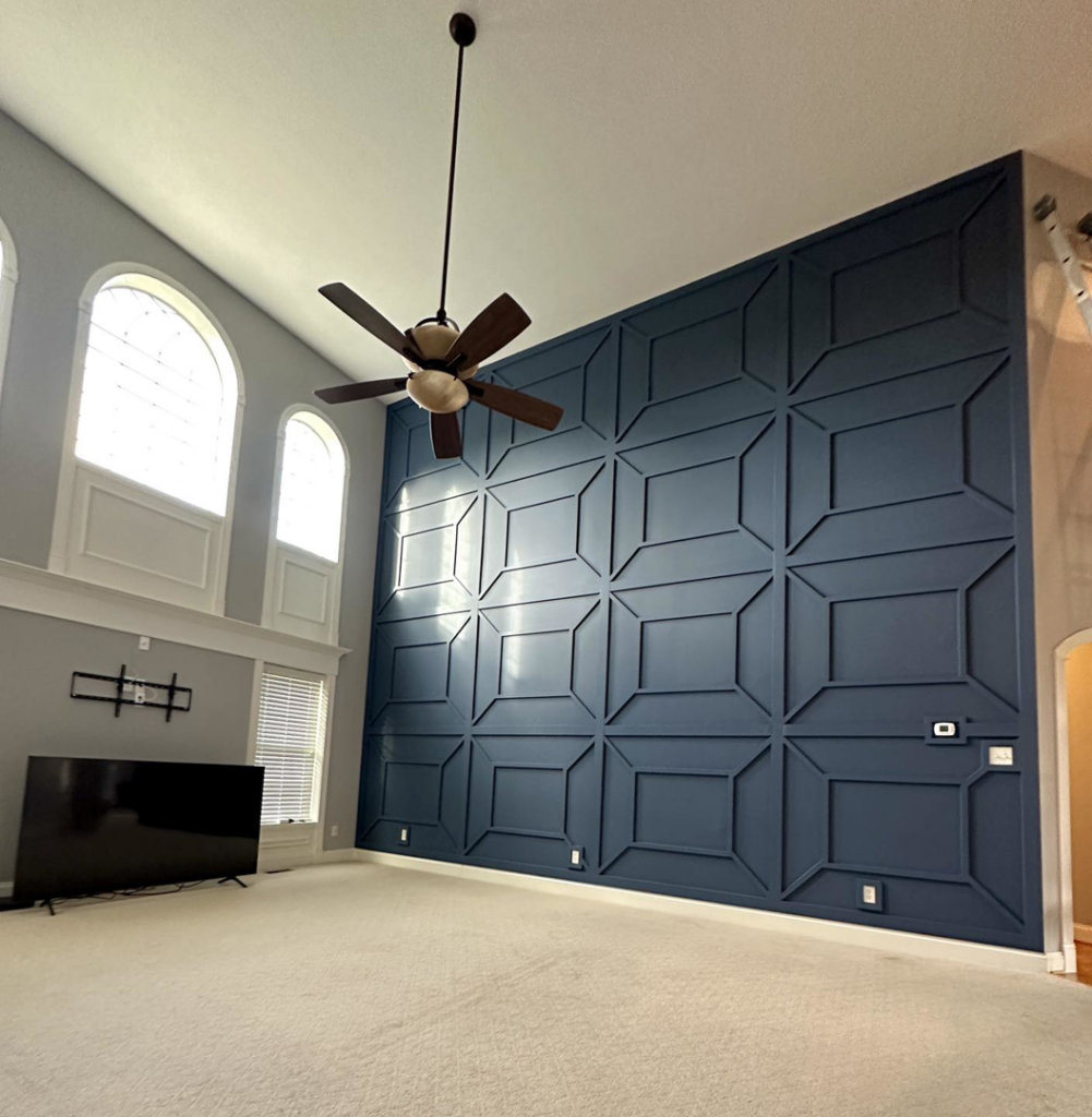 A living room featuring a tall dark blue geometric accent wall and ceiling fan by Hawkeye Painting Co. in Richmond, VA.