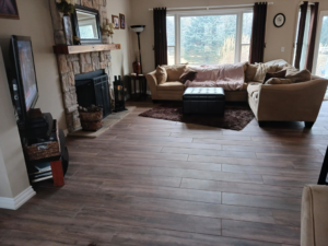A spacious living room featuring a newly installed wood-look tile floor and a stone fireplace by Home Improvement Design Center in Ann Arbor, MI.