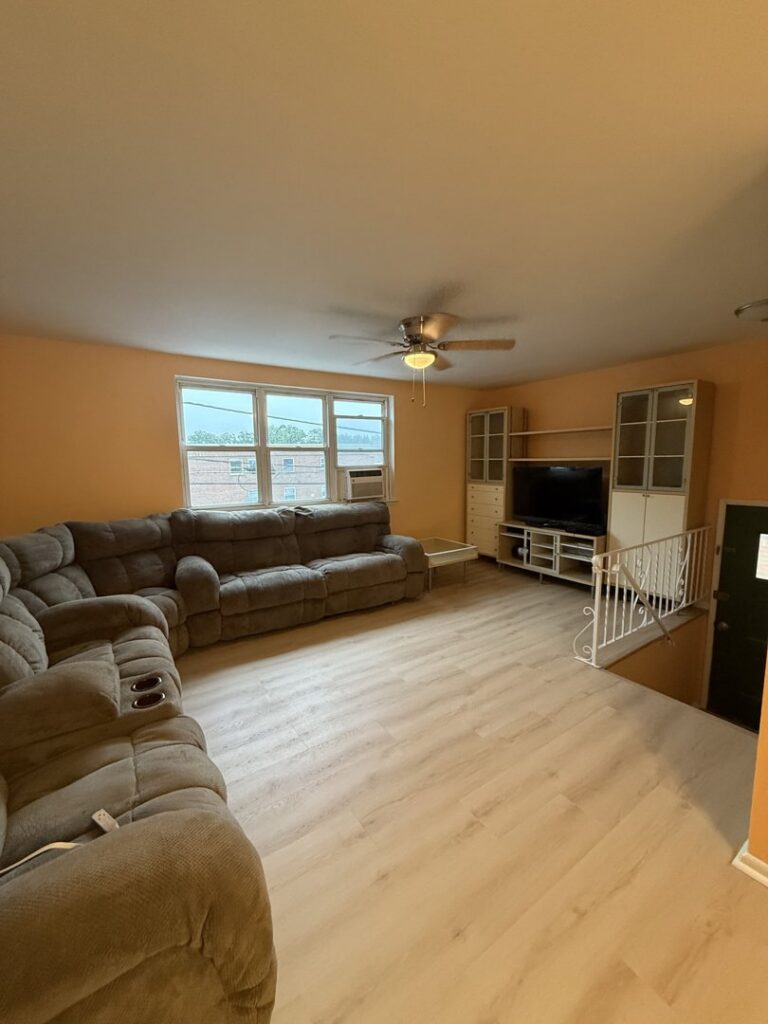 A living room featuring newly installed light laminate flooring and a large sectional sofa by MPH Design in Philadelphia, PA.
