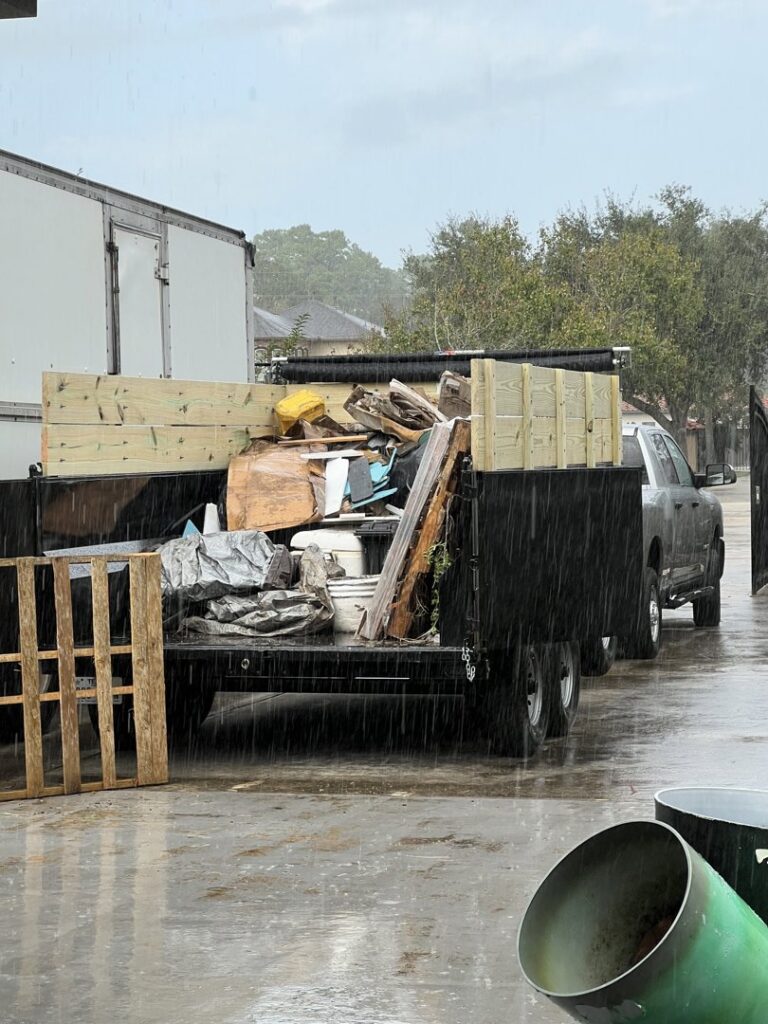 A dump trailer fully loaded with various junk and debris, parked in the rain, handled by Tidy Loaders Junk Removal in Houston, TX.