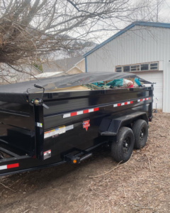 A black dump trailer with a protective tarp covering loaded items, used for junk removal by S&J Rental and Removal in Ogden, UT.