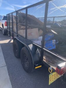A mesh-sided trailer loaded with various items and junk, ready for hauling by Discount Hauling in Las Cruces, NM.