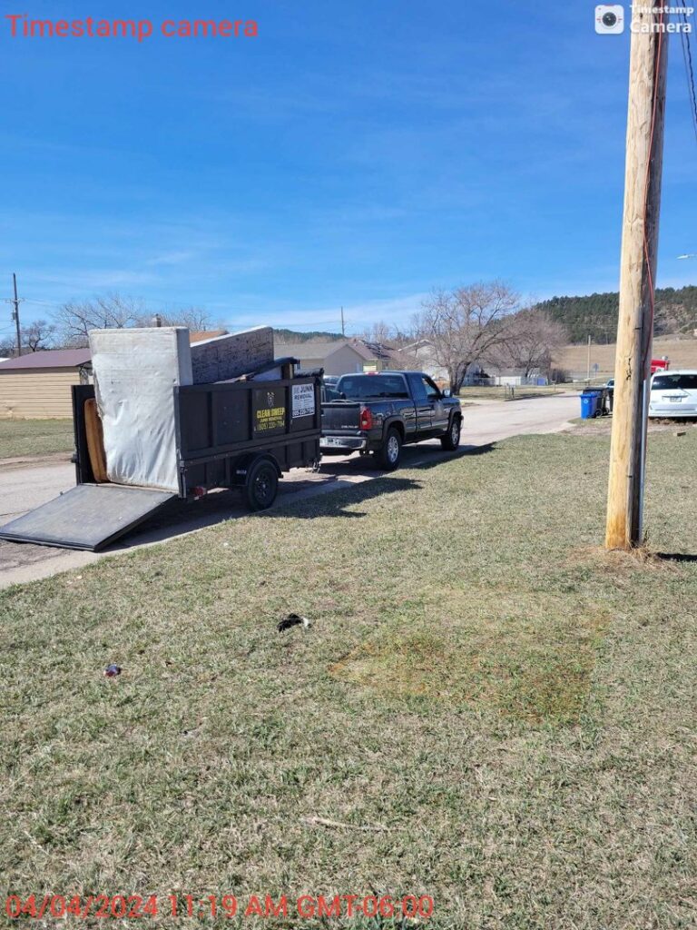 A Clean Sweep Junk Removal trailer loaded with mattresses and furniture on a residential street in Augusta, ME.