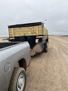 A pickup truck towing a dump trailer loaded with debris along a muddy road, providing junk removal service by Tidy Loaders in Houston, TX.