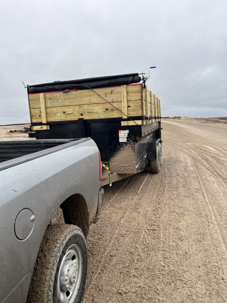 A pickup truck towing a dump trailer loaded with debris along a muddy road, providing junk removal service by Tidy Loaders in Houston, TX.