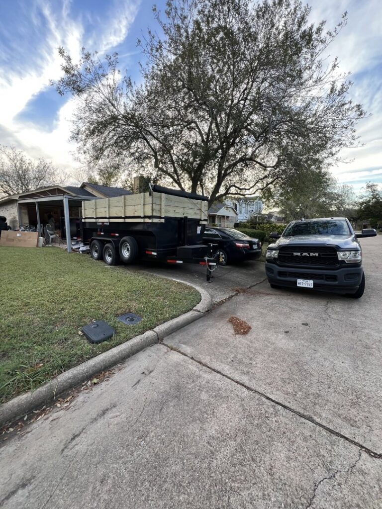 A pickup truck and a dump trailer loaded with junk parked in a residential driveway for Tidy Loaders Junk Removal in Houston, TX.