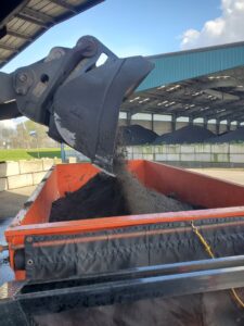 A front-end loader dumping bulk material into an orange roll-off dumpster for ADE Hauling in Tacoma, WA