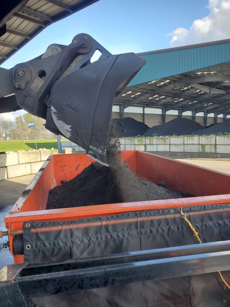 A front-end loader dumping bulk material into an orange roll-off dumpster for ADE Hauling in Tacoma, WA