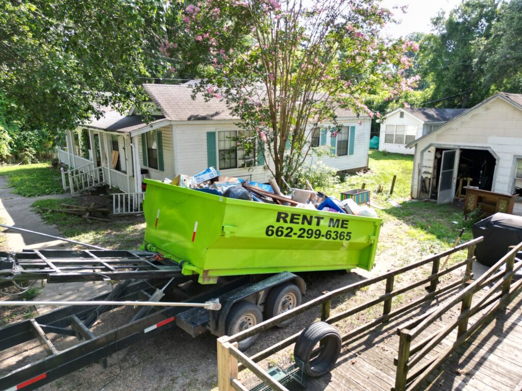 A full bright green dumpster being loaded onto a trailer for junk removal by Tristate Dumpsters LLC in Greenville, MS.