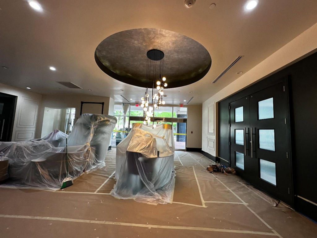 A lobby undergoing renovation with furniture covered in plastic, showing work in progress by Painting Services by David LLC in Houston, TX.