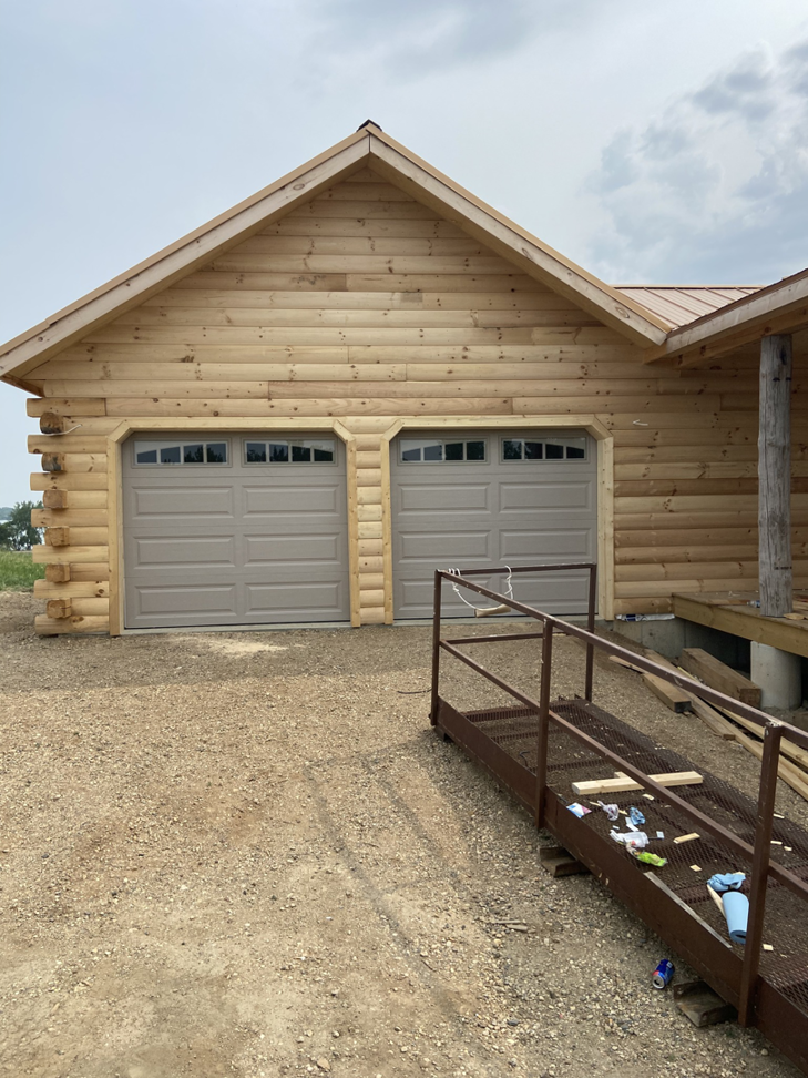Exterior view of a log cabin style house with new garage doors and a construction ramp, completed by RT Handyman LLC in Sioux Falls, SD.
