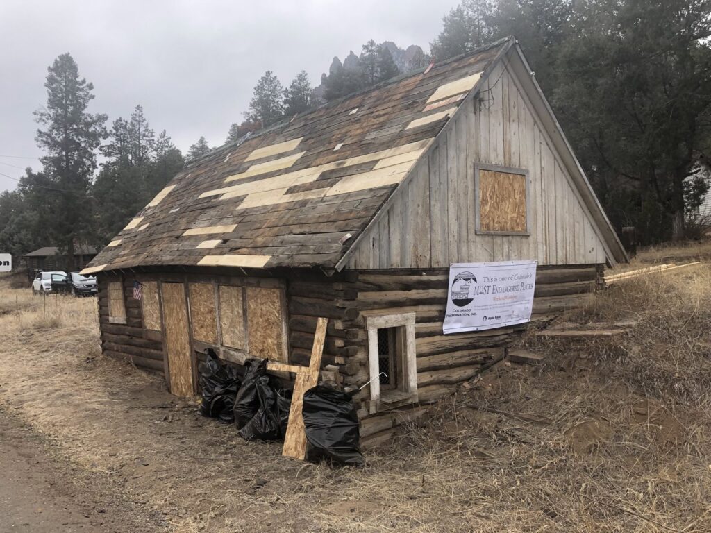 Historic log cabin undergoing restoration with roof repair and boarded windows by Deep Roots Craftsmen in Fort Collins, CO.