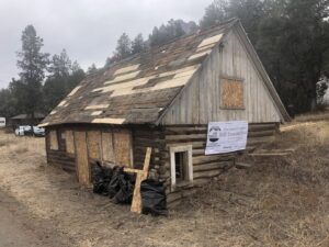 Historic log cabin undergoing restoration with roof repair and boarded windows by Deep Roots Craftsmen in Fort Collins, CO.