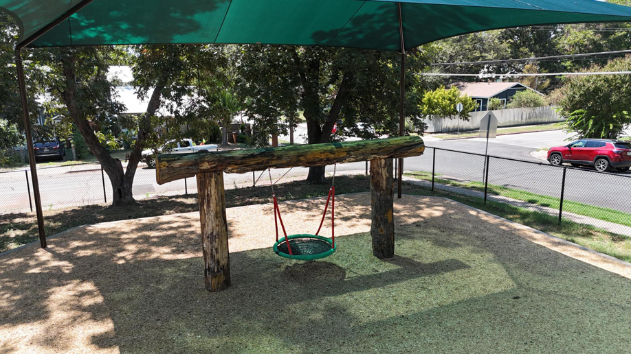 Log swing set under a green shade structure in a playground built by Paradigm Contracting LLC in Wichita, KS.